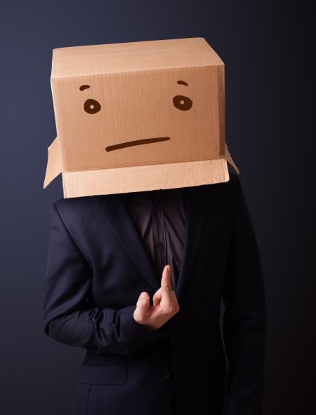 Young man standing and gesturing with a cardboard box on his head with straight face