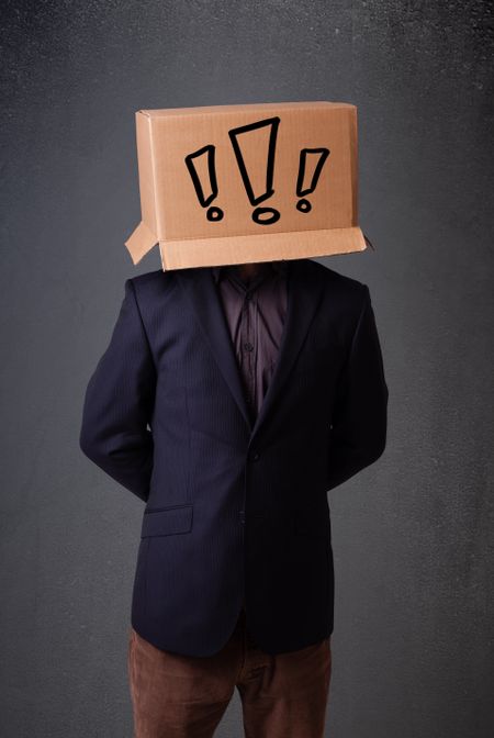 Young man standing and gesturing with a cardboard box on his head with exclamation point
