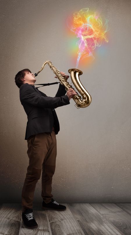Attractive young musician playing on saxophone with colorful abstract fume comming out