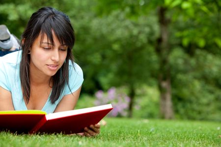 Beautiful young woman reading a book outdoors