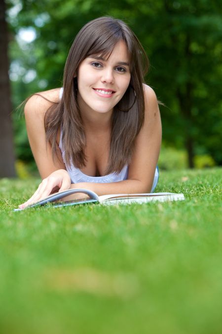 Beautiful girl reading a book outdoors and smiling