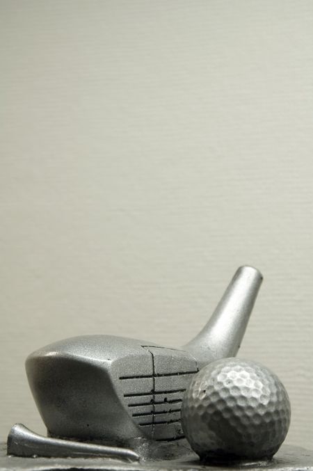 Golf trophy - silver-coated driver head, tee, and ball - with beige paper background inside trophy case