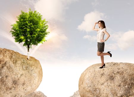 Businesswoman standing on the edge of rock mountain with a tree on the other side 