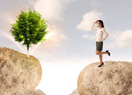 Businesswoman standing on the edge of rock mountain with a tree on the other side