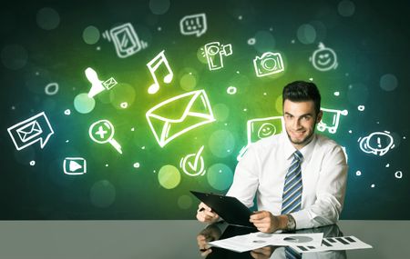 Businessman sitting at the black table with social media symbols on the background