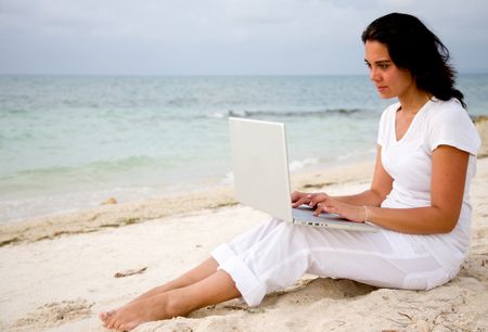 Beautiful woman at the beach working on a laptop
