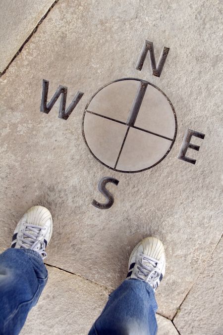Two feet standing by directional map in stone, north south east west