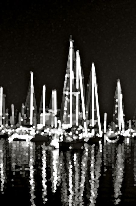 Black and white nocturnal abstract of sailboats with glowing masts and reflections together in a tropical marina (one of a series)