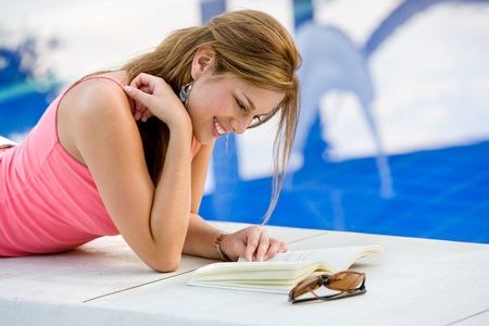 Beautiful woman reading a book by the swimming pool