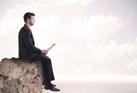 A young sales person in elegant suit sitting with paper on top of a stone in the clouds concept