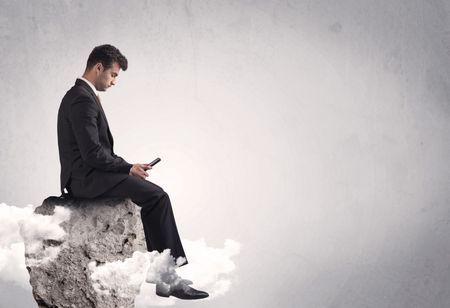 An elegant  smart businessman with laptop sitting in empty grey space on top of a cliff, between clouds concept