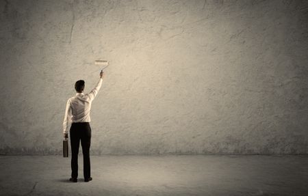 An elegant businessman in suit holding a paint roller, standing with his back, facing an empty urban concrete wall concept