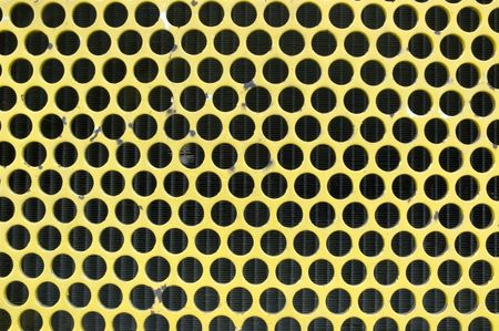 Yellow grill in front of radiator coils of earth mover, full-frame close-up