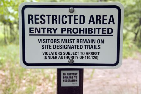 Warning sign by trail in state park: RESTRICTED AREA . . . VIOLATORS SUBJECT TO ARREST . . .