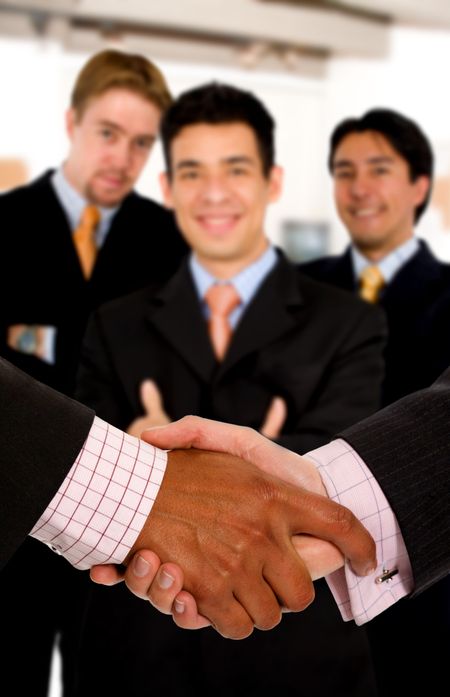 Business deal at the office - team of businessmen behind a handshake