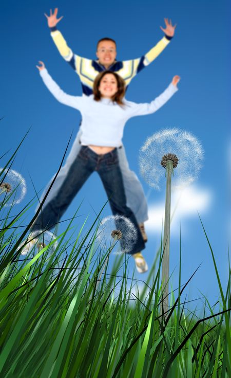 Couple having fun jumping outdoors with the focus in the foreground grass and flowers