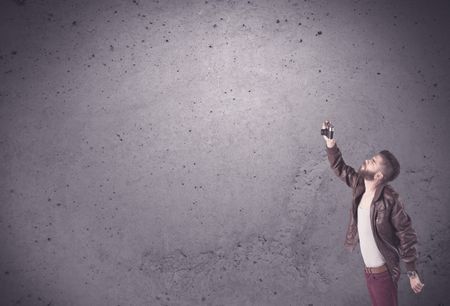 A stylish funny hipster person holding a vintage camera and taking photographs in front of a concrete clear empty urban wall background concept