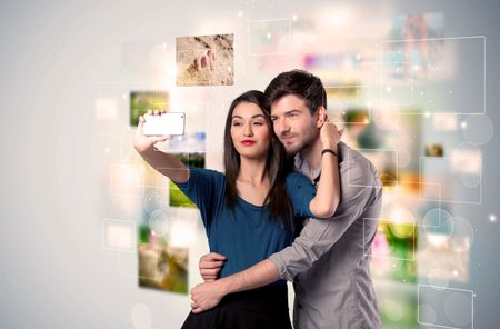 Collecting memories concept with photos in backbround and a happy young couple in love taking selfie with a mobile phone