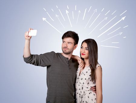 A cheerful young couple taking selfie photo with mobile phone and white lines and arrows pointing to the sky above them concept