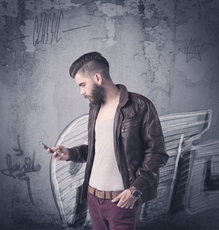 A handsome hipster guy with beard and sunglasses standing in front of an urban wall with graffiti concept