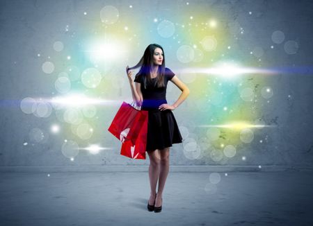 A beautiful young girl standing with long hair and red shopping bags in front of colorful light bokeh urban wall background concept