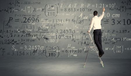 A businessman in elegant suit standing on a small ladder and writing numbers, calculating on grey wall background