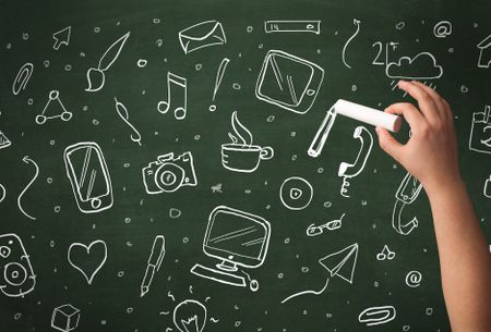 A person drawing media and communication icons on school blackboard with chalk