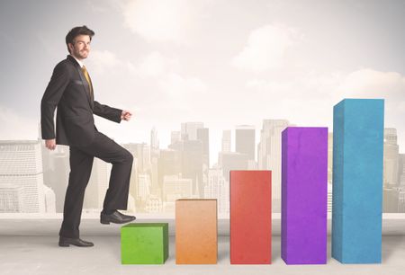 Business person climbing up on colourful chart pillars concept on city background