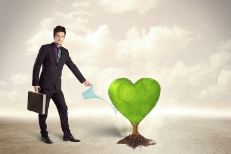 Business man watering heart shaped green tree concept on background