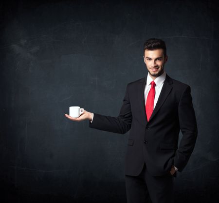 Businessman standing and holding a white cup on a black background

