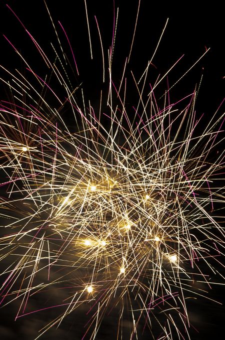 Multiple fireworks bursts near one another, with many crisscrossing streaks