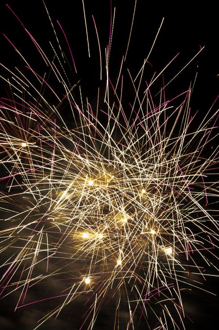 Multiple fireworks bursts near one another, with many crisscrossing streaks