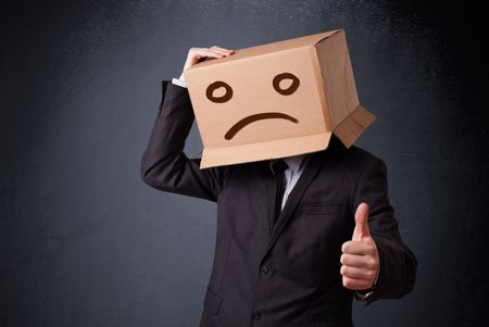 Businessman standing and gesturing with a cardboard box on his head with sad face