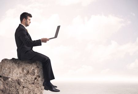 A young sales person in elegant suit sitting with paper on top of a stone in the clouds concept