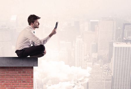 An elegant businessman in modern suit sitting on the top of a brick building, looking over the cityscape with clouds concept
