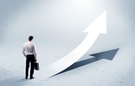 A young adult salesman standing in front of a big arrow pointing up with a shadow in grey empty space concept