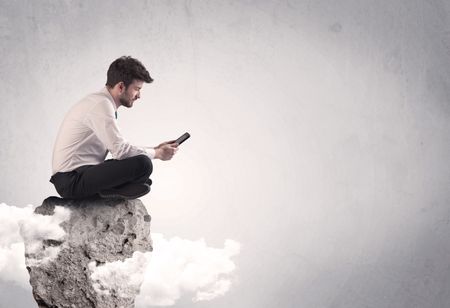 An elegant  smart businessman with laptop sitting in empty grey space on top of a cliff, between clouds concept