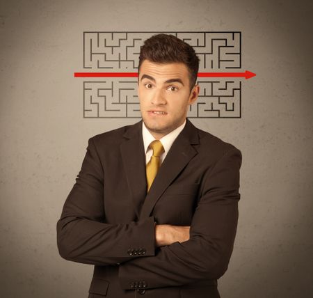 A young handsome business person making facial expression and solving maze with red arrow in front of clear, empty concrete wall background concept