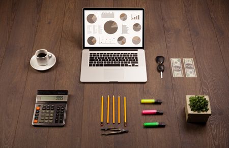 Pie chart graph icons and symbols on laptop screen with office accessories