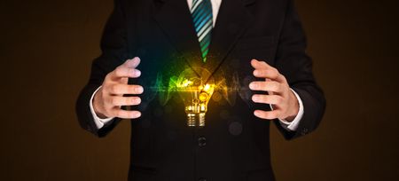 Businessman holding a shining light bulb in front of his body
