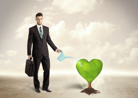 Business man watering heart shaped green tree concept on background