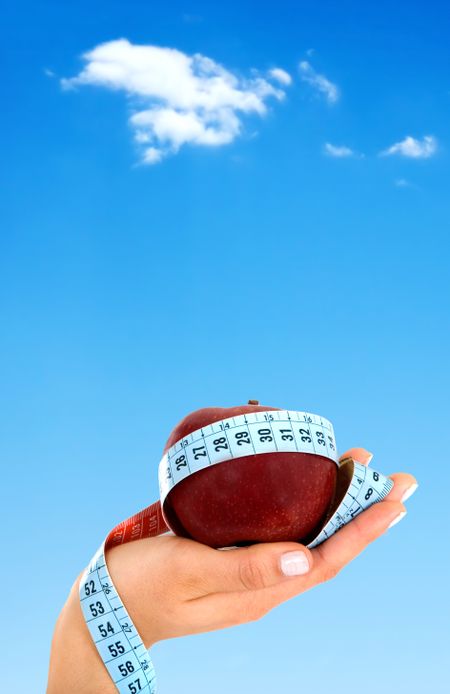 hand holding an apple with a tape measure over a beautiful blue sky in the background