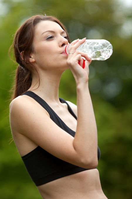 Athletic woman drinking water after exercising outdoors