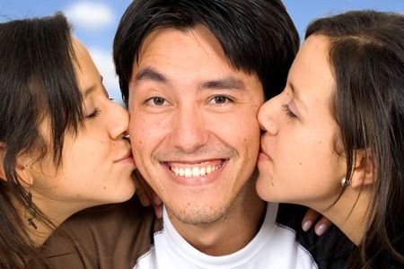 twin girls kissing a guy who is looking very happy with a blue sky in the background