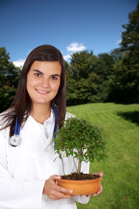 Smiley female doctor with a tree outdoors