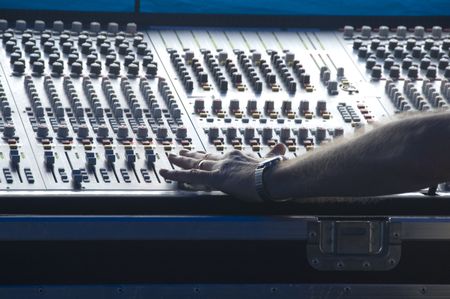 Technician's left hand makes adjustment on audio control panel in booth at outdoor concert