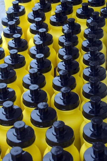 Many identical yellow water bottles with black caps in daylight