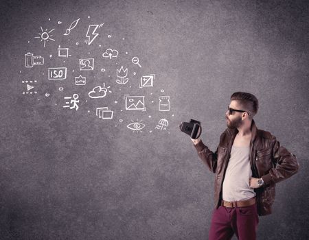An elegant hipster guy trying to use a vintage camera with camera settings icons drawn on wall, like flash, white balace or ISO value concept