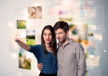 Collecting memories concept with photos in backbround and a happy young couple in love taking selfie with a mobile phone