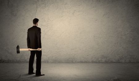 Business man standing in front of a grungy copyspace wall with a hammer